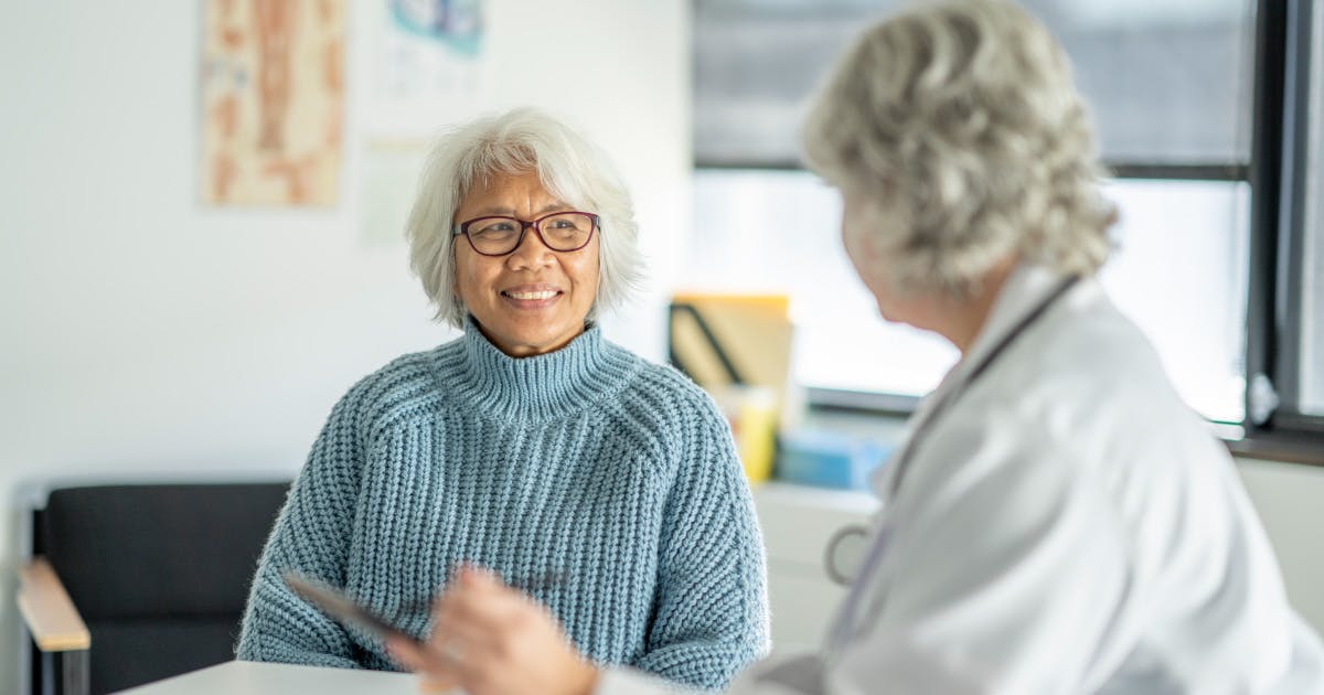 A smiling older woman talks to a doctor.