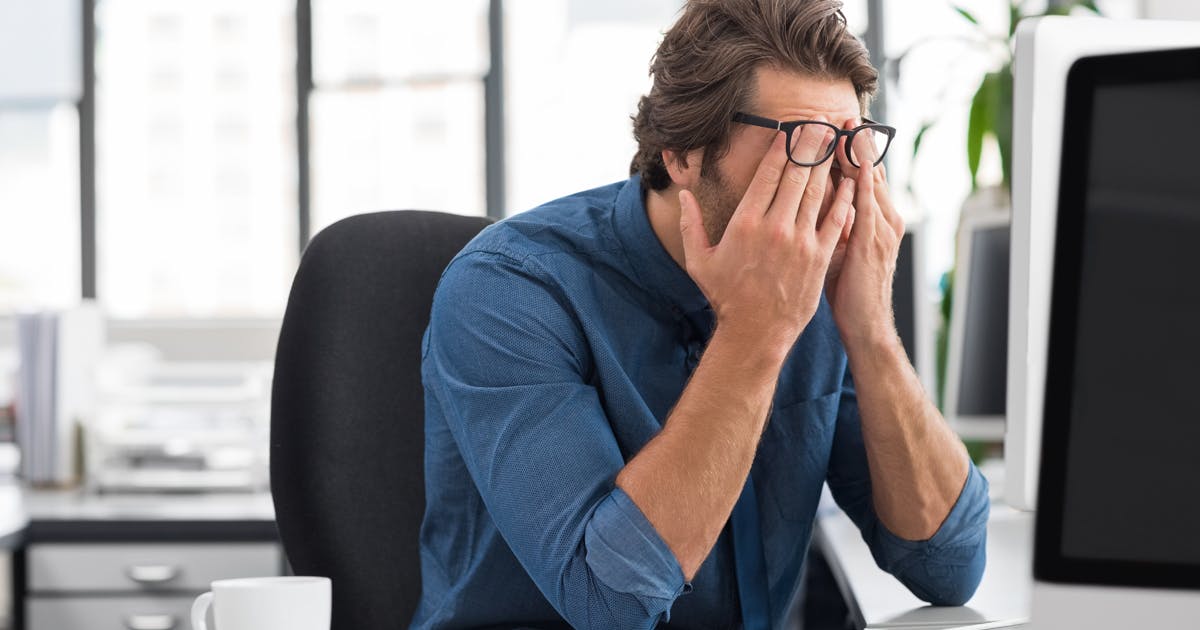 A man in an office rubs his eyes.