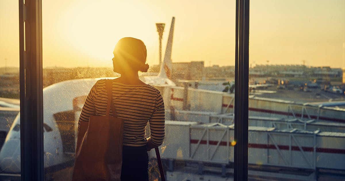 A woman standing in an airport and looking out a window at an airplane.
