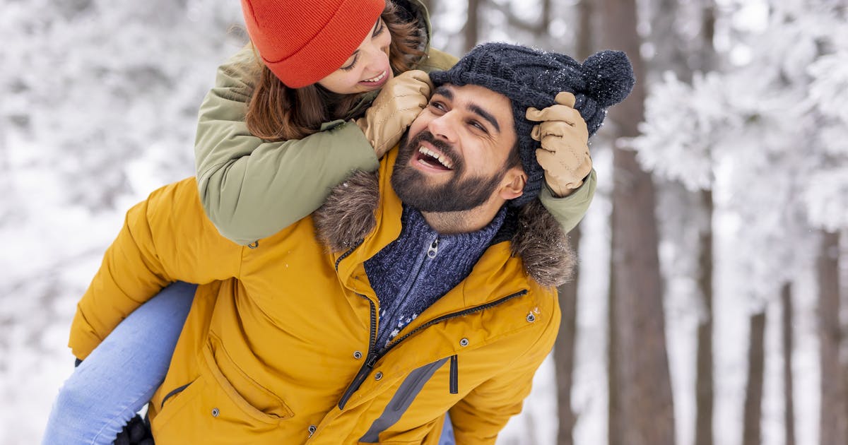 A man gives a woman a piggyback through snowy woods