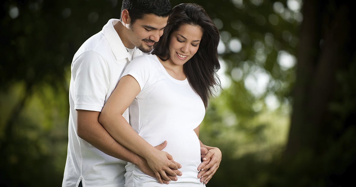  A man and a pregnant women place their hands on her belly.