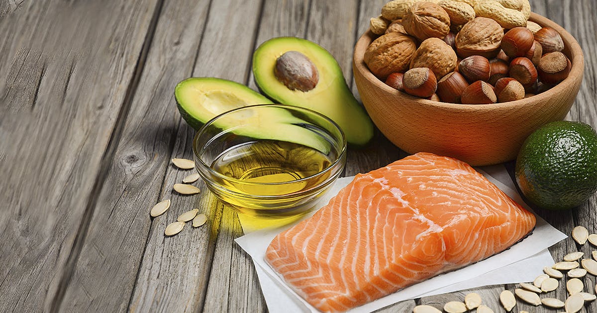 Salmon, avocados, oil, nuts and seeds on a wooden table.