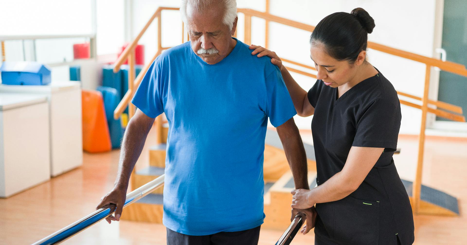 A physical therapist helps an older man with a walking exercise.