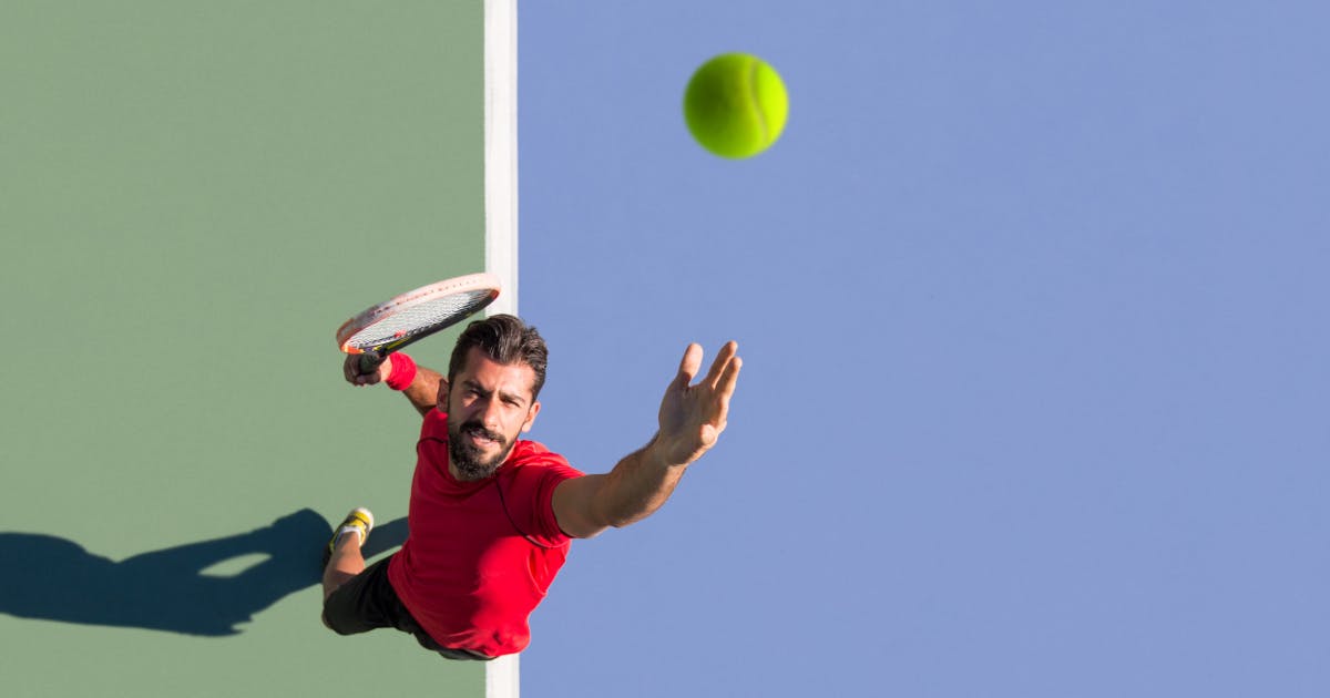 A tennis player tosses a ball up for a serve.