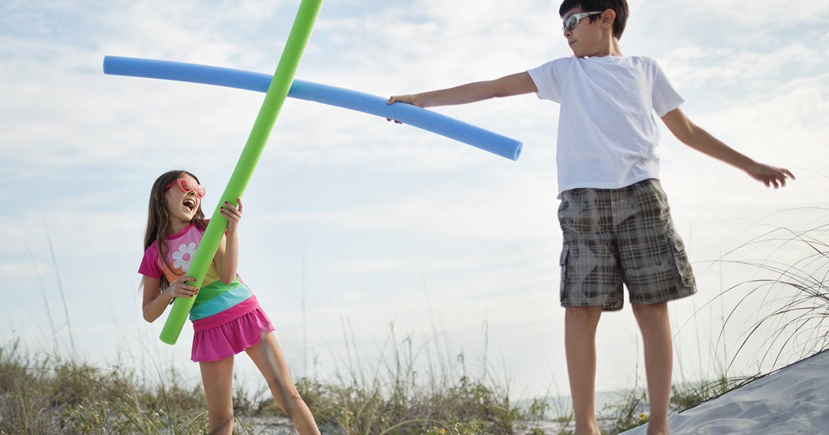 Two kids fencing with pool noodles.