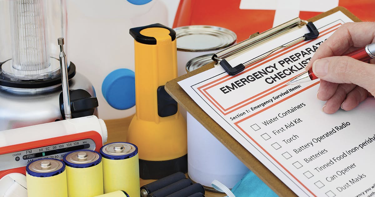 An emergency checklist on a clipboard with batteries, a radio, a flashlight and other supplies.