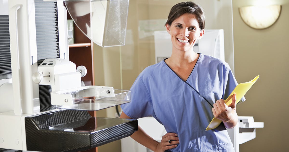 A mammogram technician standing next to a mammogram machine.