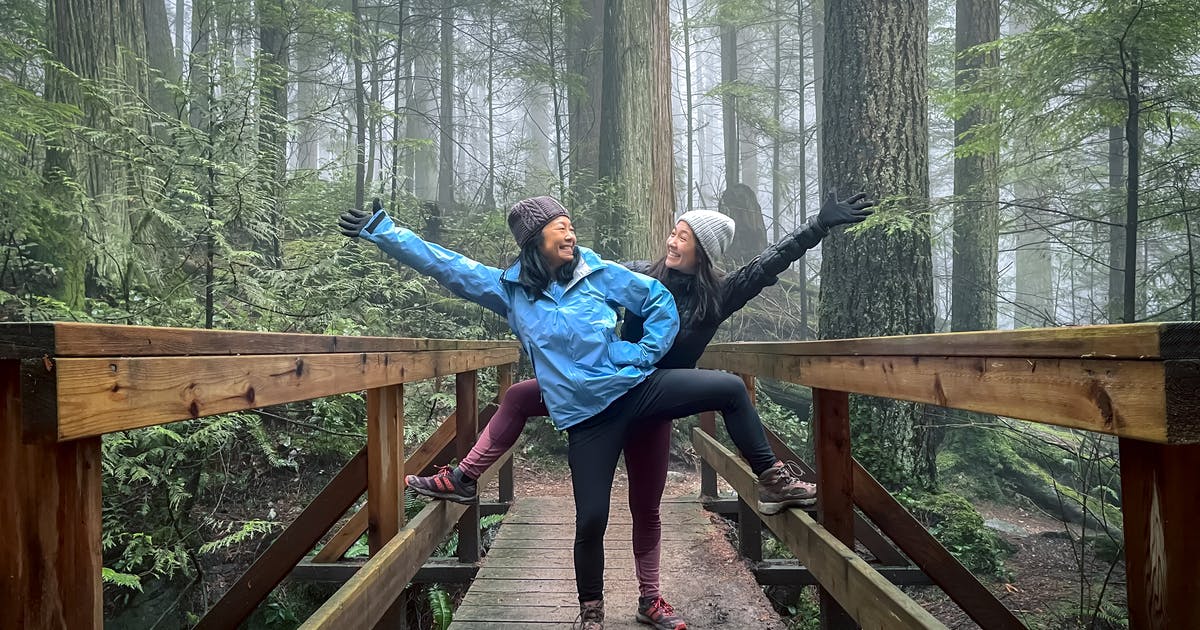 Two women in winter hiking clothes pose on a wooden footbridge.