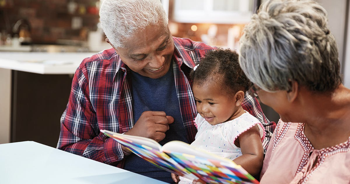 A grandma and grandpa read to their baby granddaughter. 