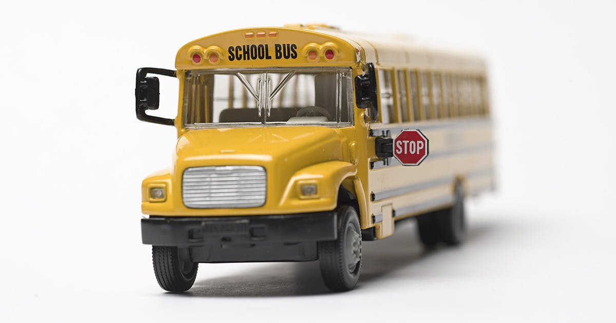 A yellow toy school bus with its stop sign extended, all on a white background. 