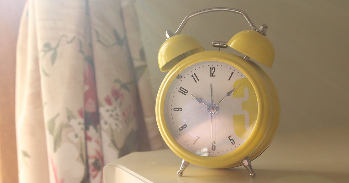 A vintage yellow alarm clock sits on a bedside table.