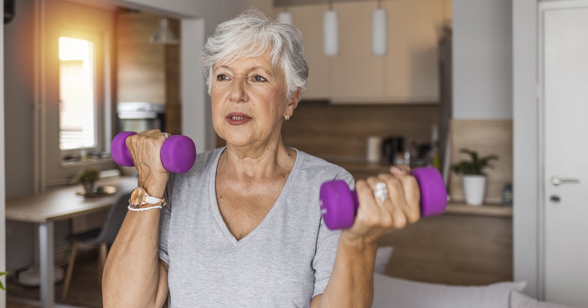 A woman holds up a pair of hand weights.