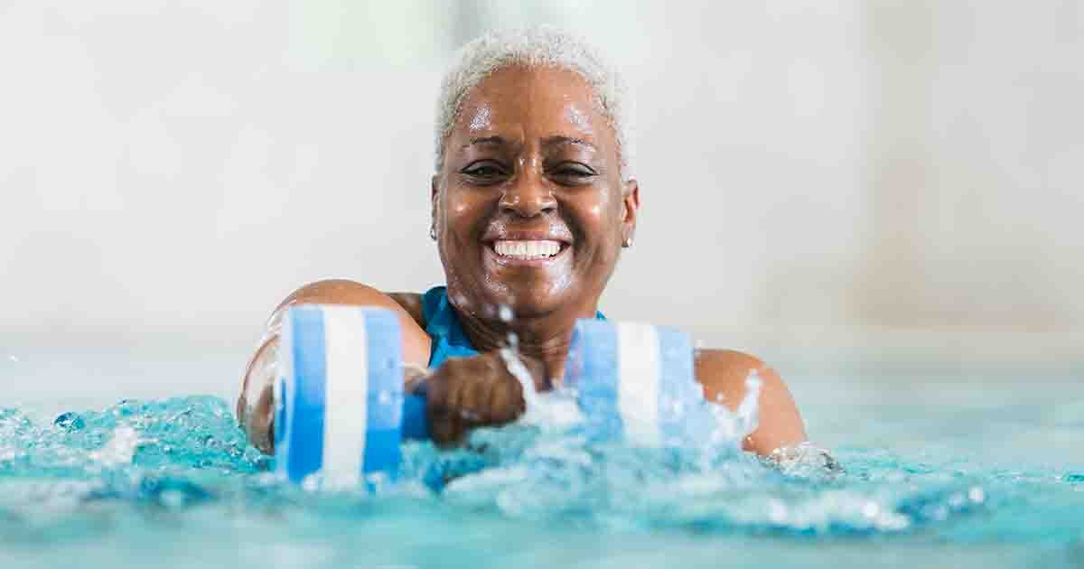 Older woman in pool smiling, doing water aerobics.