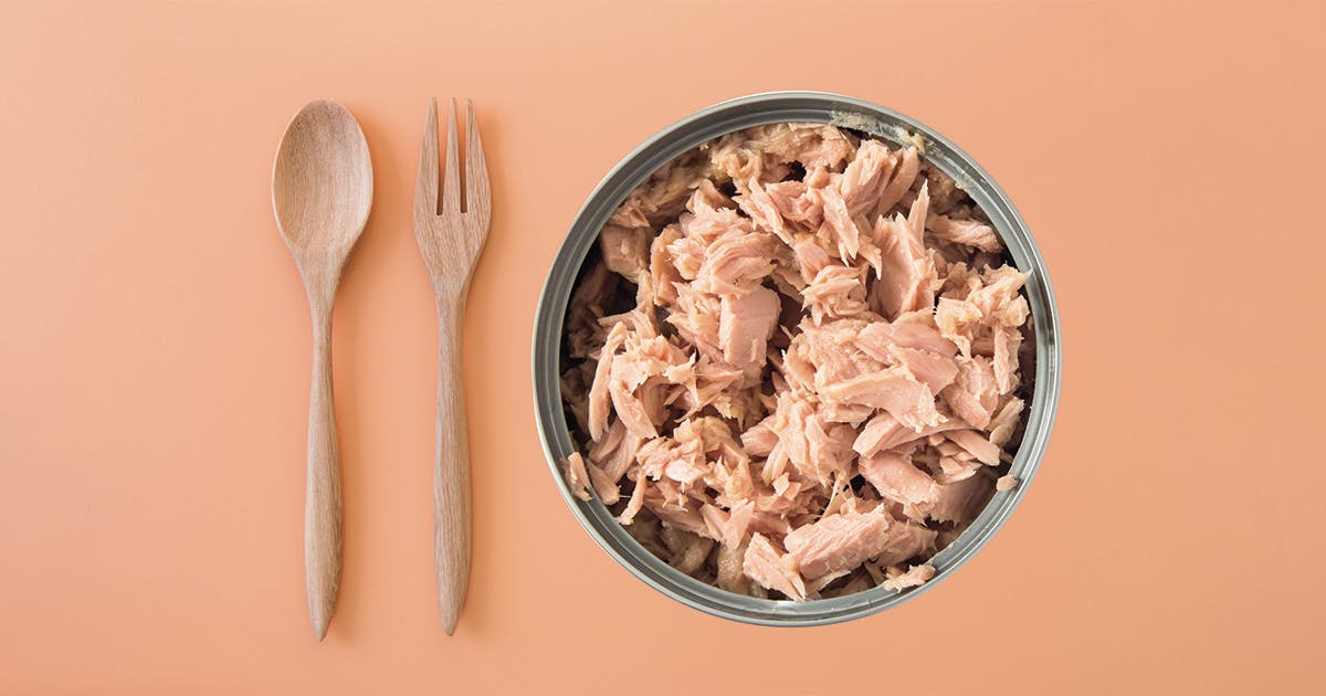 A bowl of tuna fish with a fork and spoon next to it.