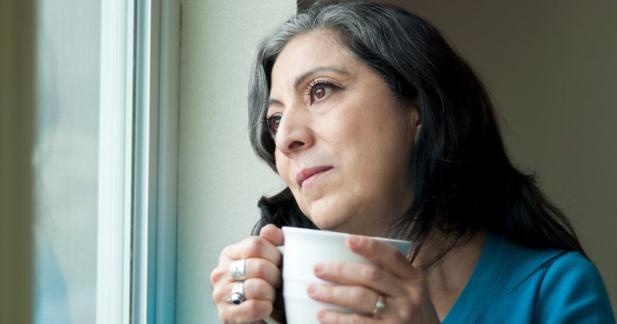 A woman holding a mug looks out a window