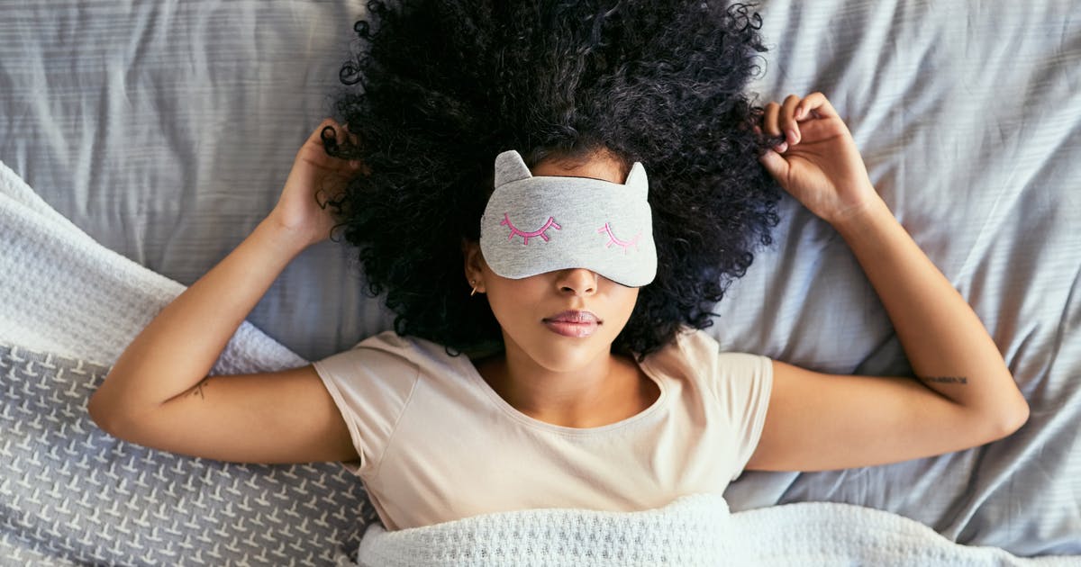 A woman lies in bed with a sleep mask over her eyes. 