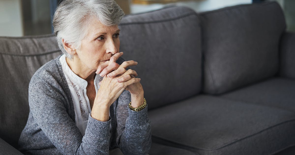 An older woman sits on a couch looking sad.