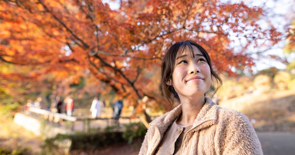 A woman smiles up at an autumn sky