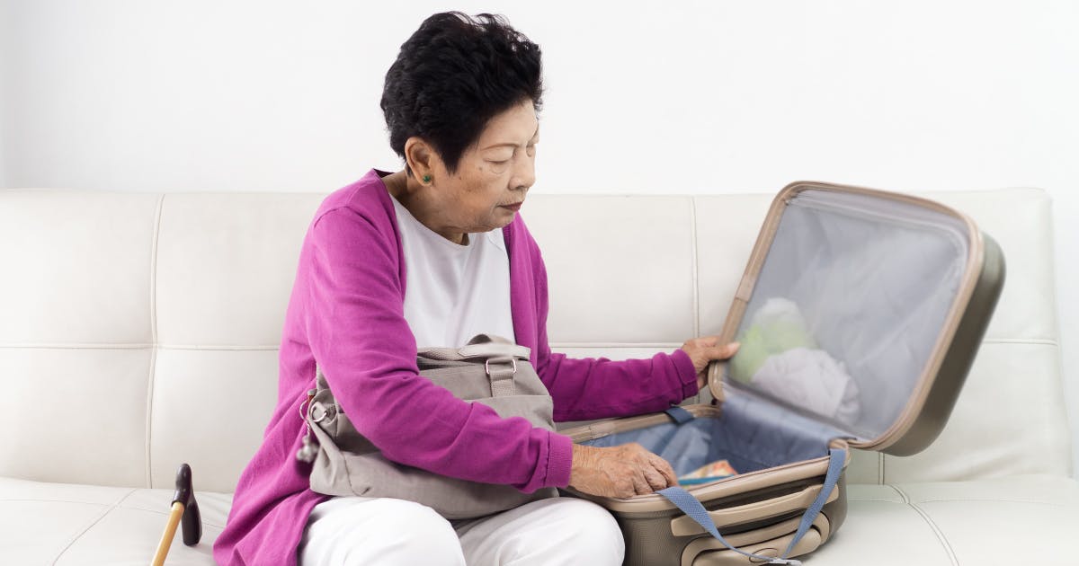 Elderly woman sitting on couch and packing luggage.