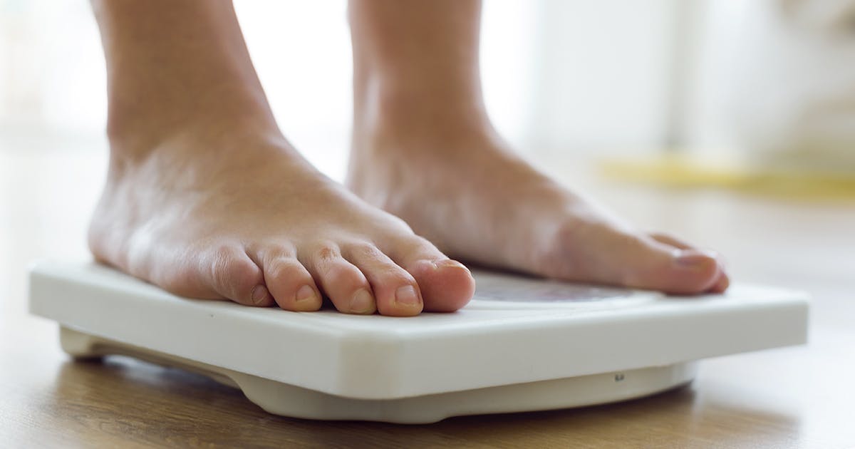 A pair of feet stand on a white bathroom scale. 
