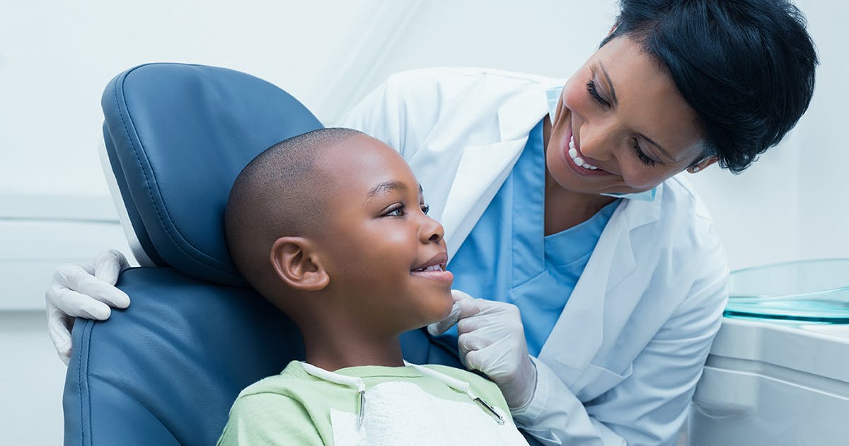 A boy smiles as he leans back in an exam chair. His dentist smiles back.