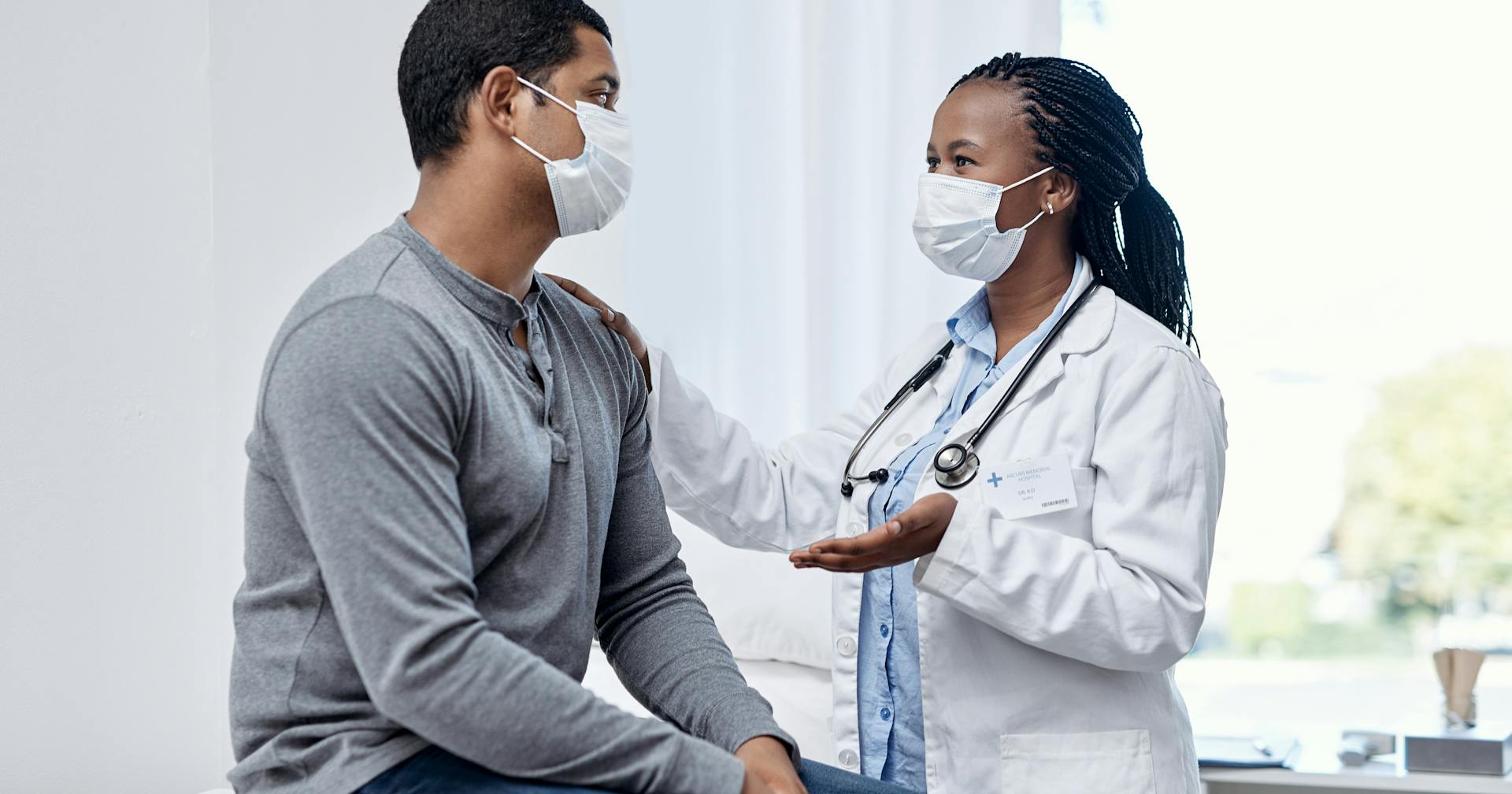 A masked patient talks to a masked doctor.
