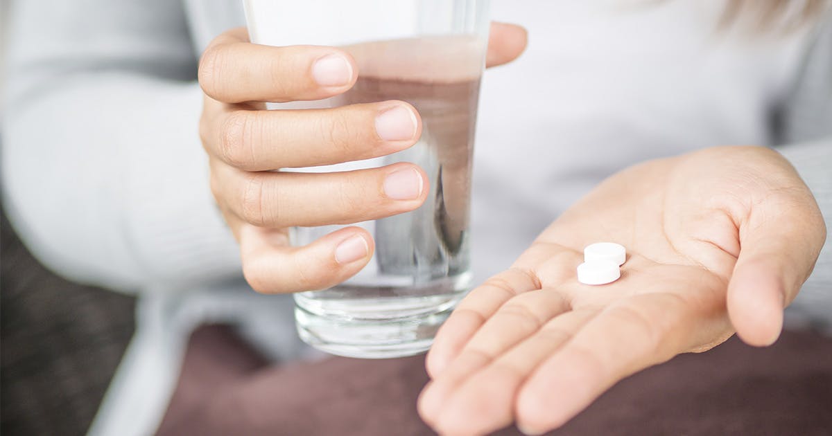 A pair of hands holding a glass of water and two white tablets.