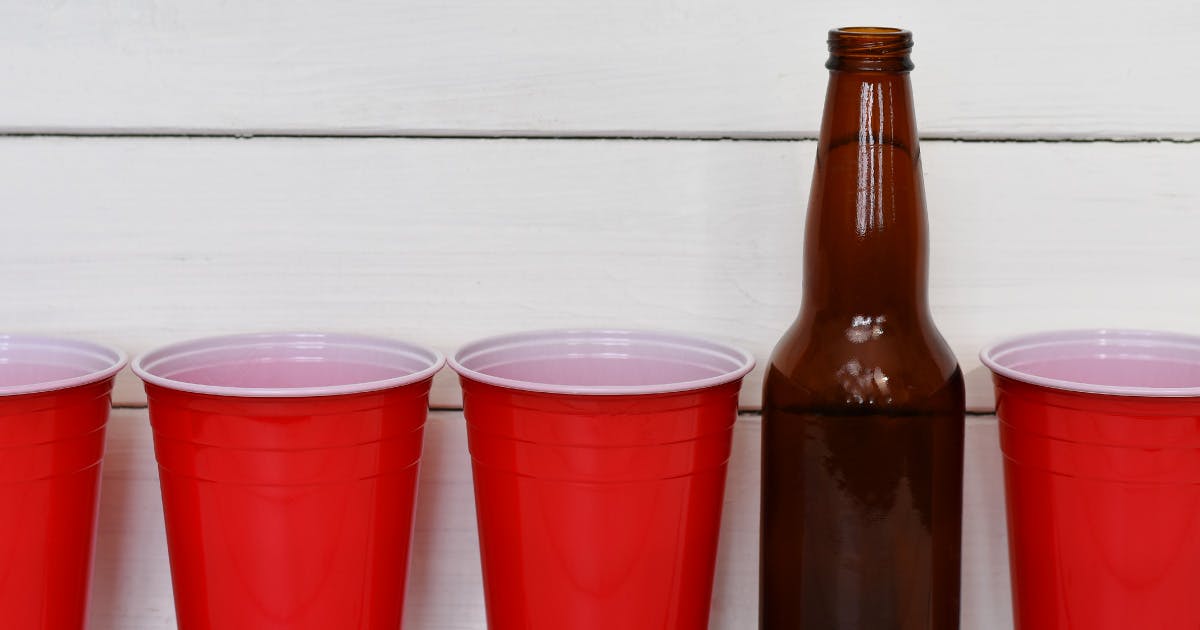 A row of empty red plastic cups and an empty beer bottle