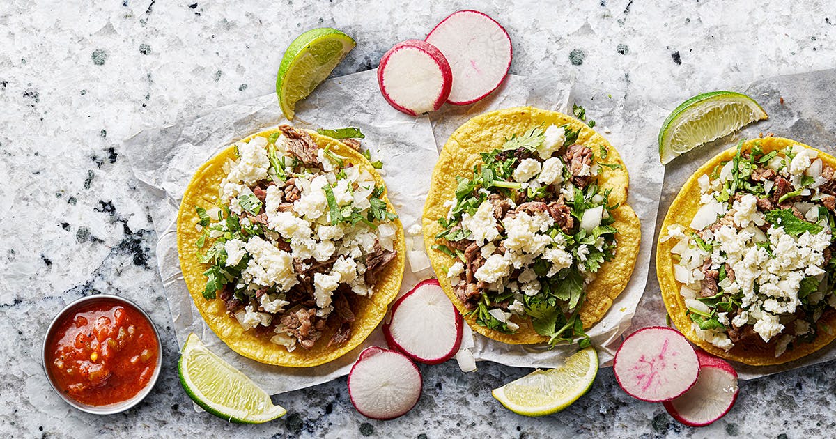 Tostadas topped with meat, lettuce and queso fresco surrounded by limes, radishes and salsa.