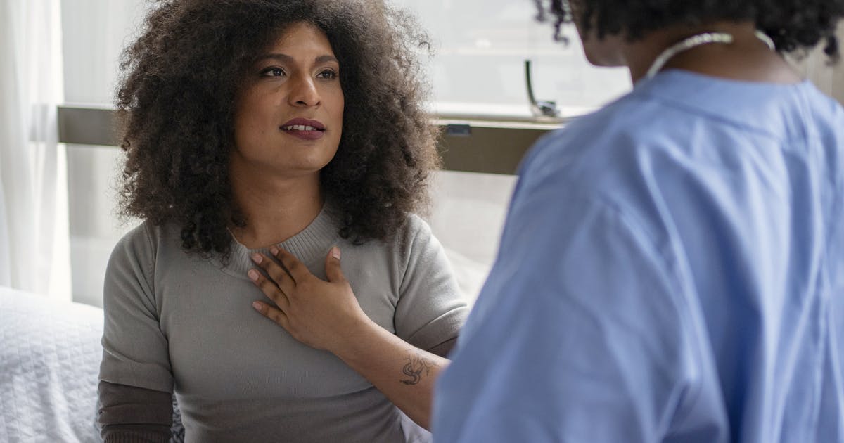 A woman holds her hand to her chest as she talks to her doctor