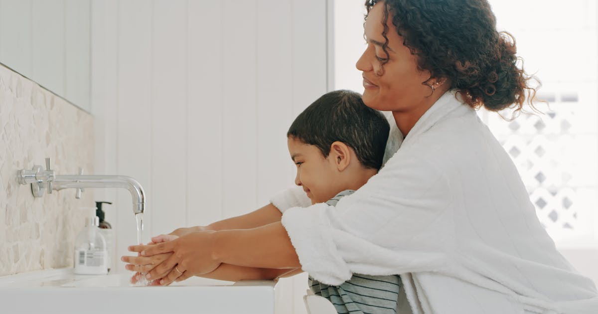 A woman helps a young boy wash his hands.