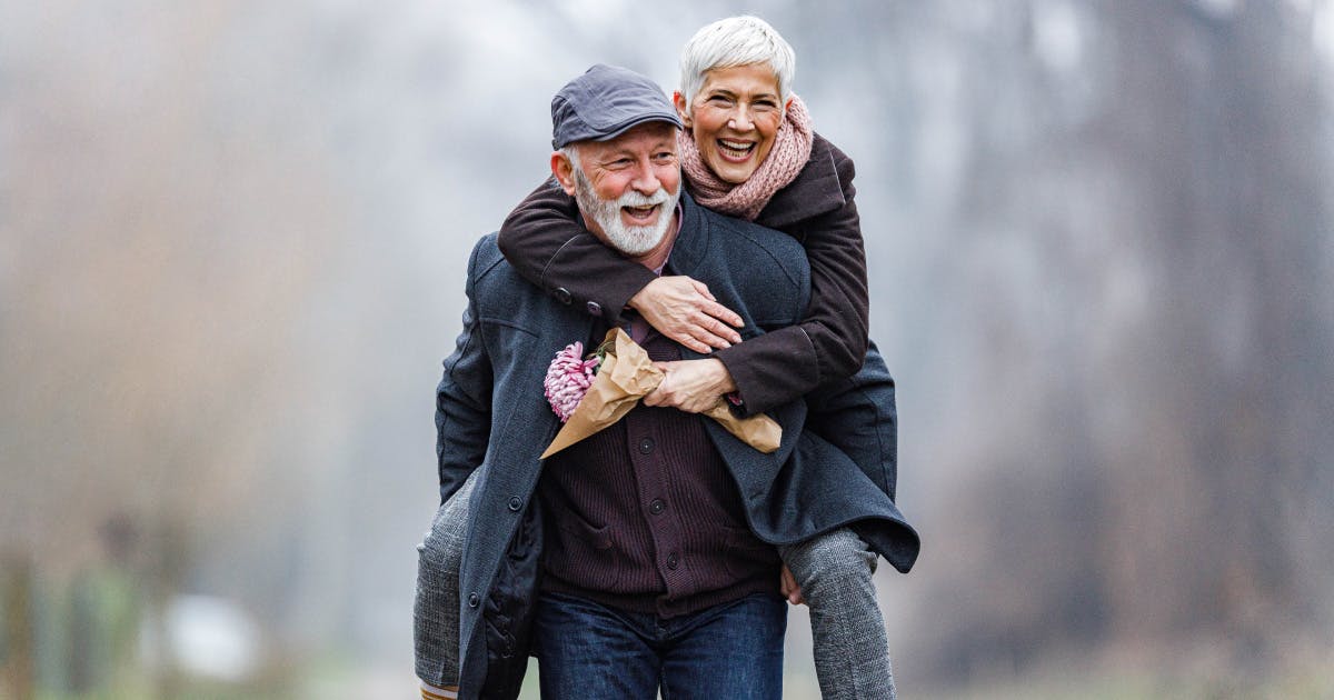  Two warmly-dressed seniors laugh outdoors.