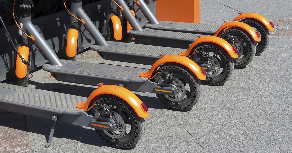 Five orange and black electric scooters sit in a row. 
