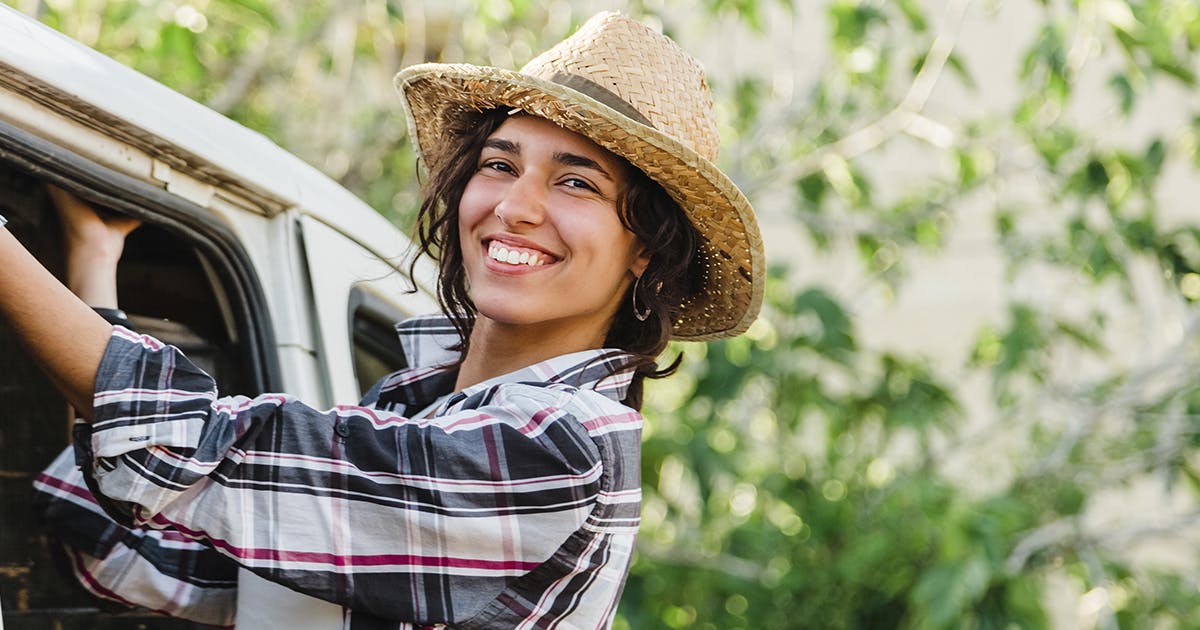 A woman in a straw hat leans out of a van.