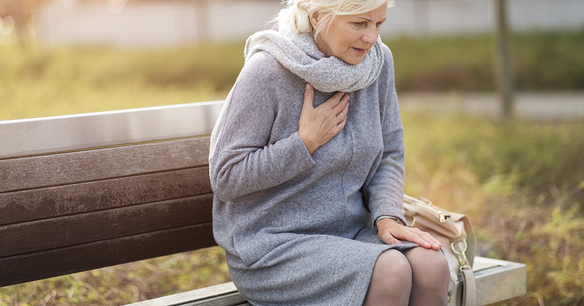 A woman sitting on a bench with her hand over her heart.