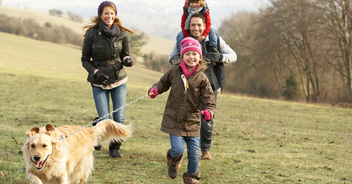 A mom, dad and two girls dressed in winter clothing running outside with their dog.