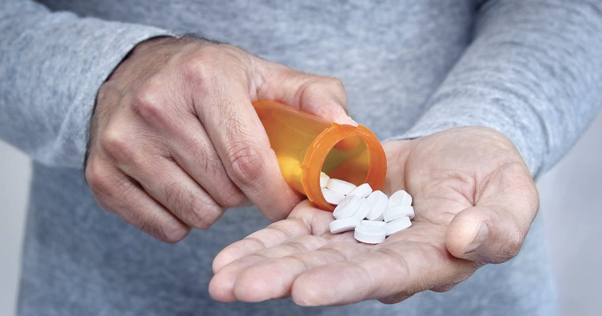 A person holds handful of prescription pills in their palm.