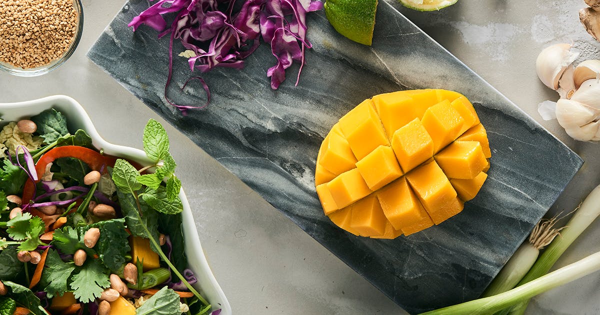A mango on a cutting board with salad ingredients.