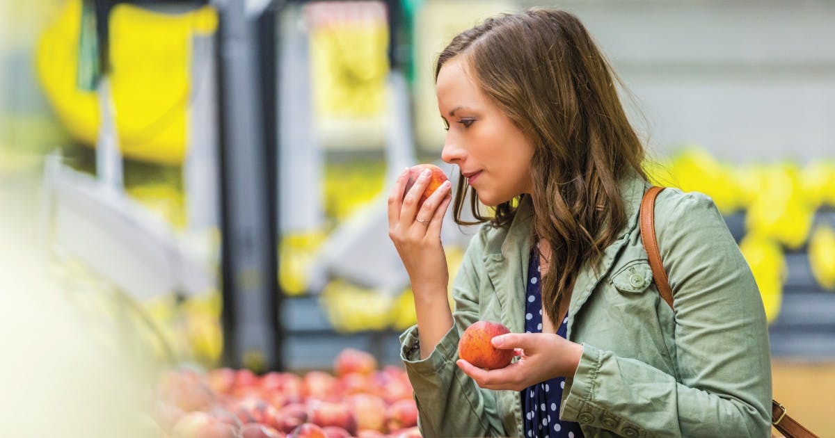 A woman smells a peach from a bin.