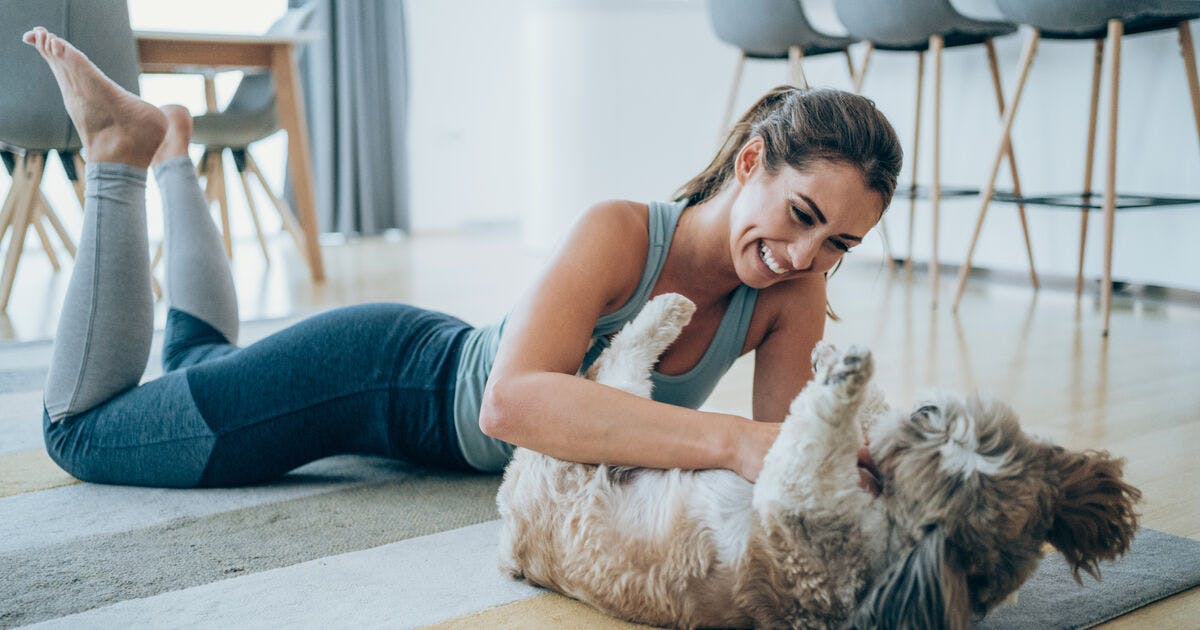   A woman plays with her dog on the living room rug