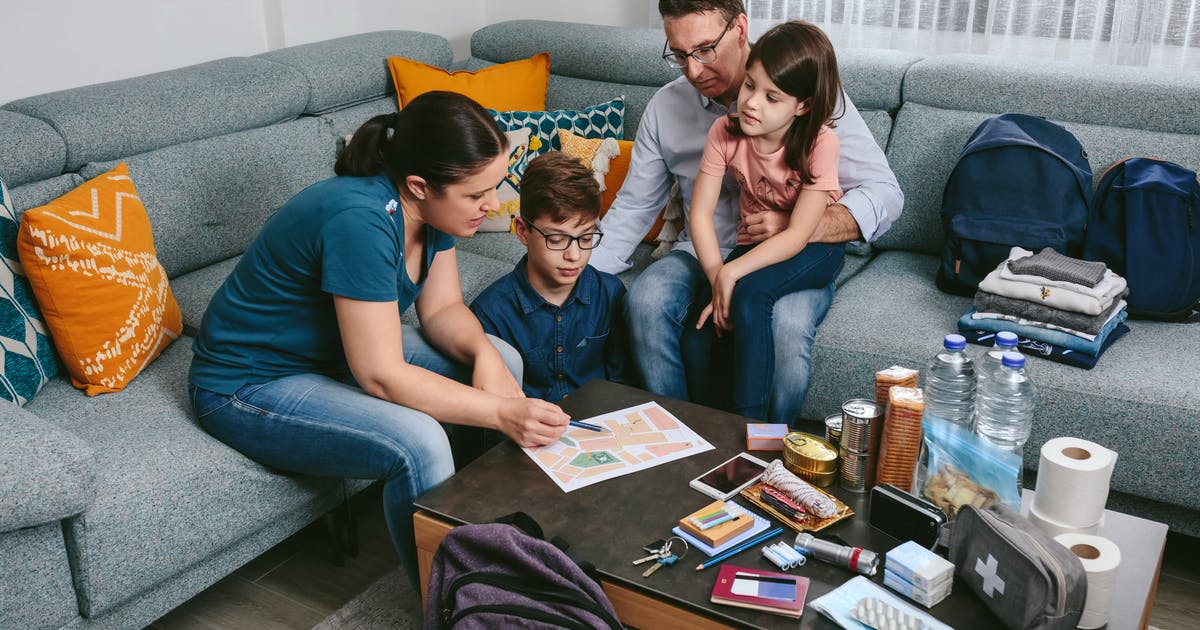  A family gathers on a couch to look at a map. An emergency kit is open on the table.