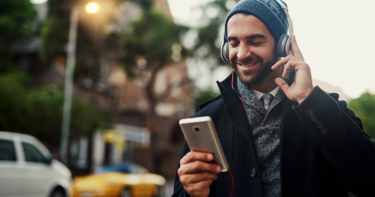 A man wearing headphones smiles at his smartphone.