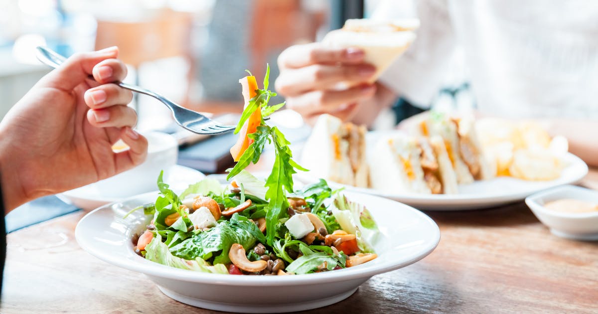 Close-up of a forkful of salad above a restaurant salad bowl.