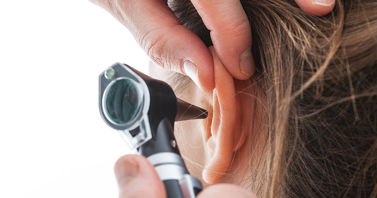 A doctor is using a scope to look inside a woman's ear.