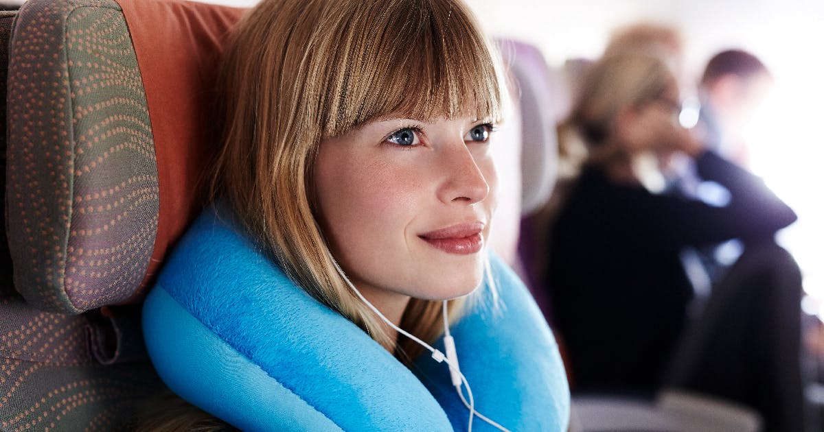  A woman on an airplane using a neck pillow.