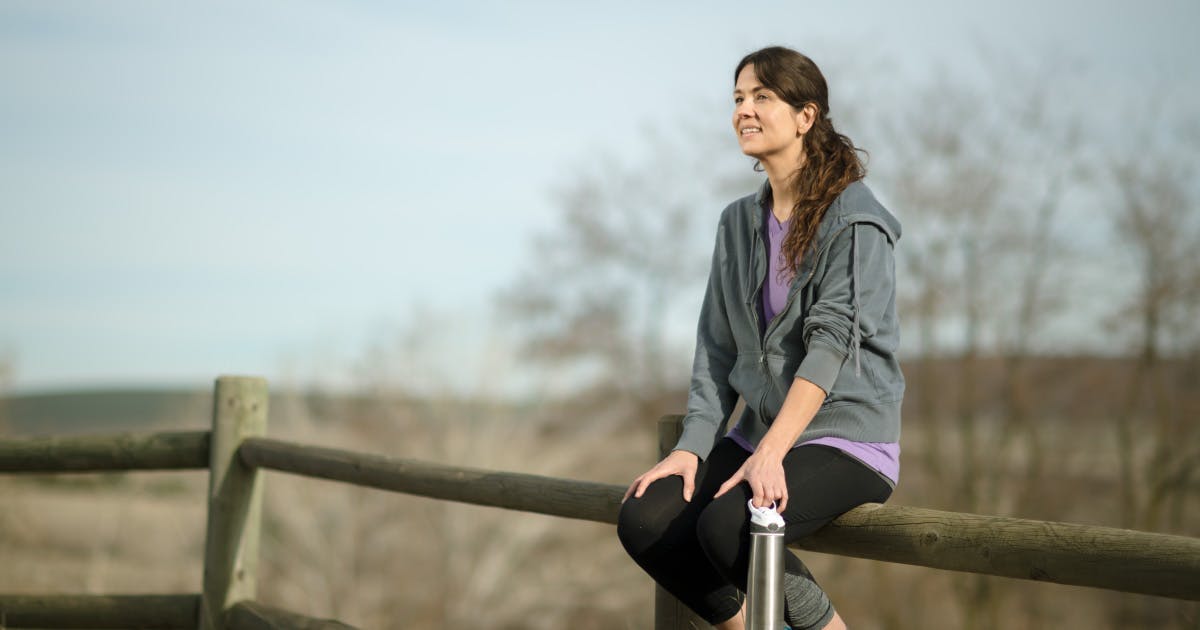 A woman sits on a wooden fence rail