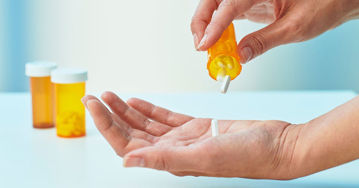A person pours white tablets from a prescription bottle into their palm.