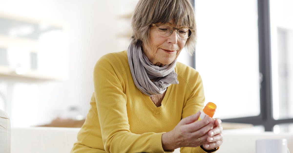 A woman on a couch looking at a prescription pill bottle