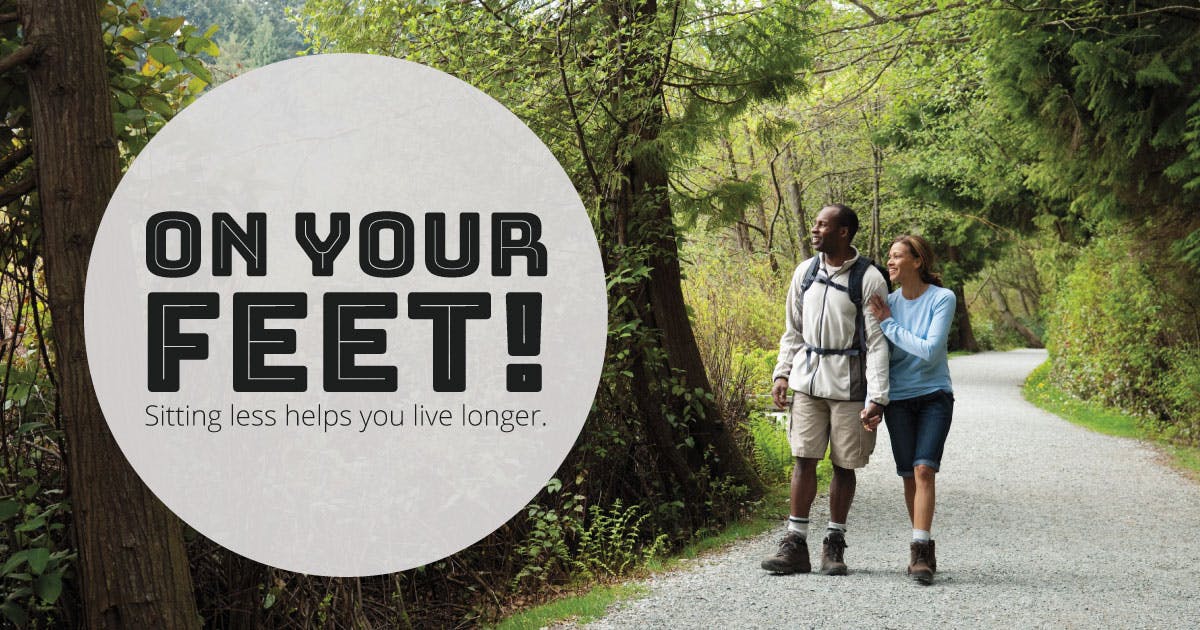 A couple hikes down a gravel trail in the woods. Text says: "On your feet! Sitting less helps you live longer."