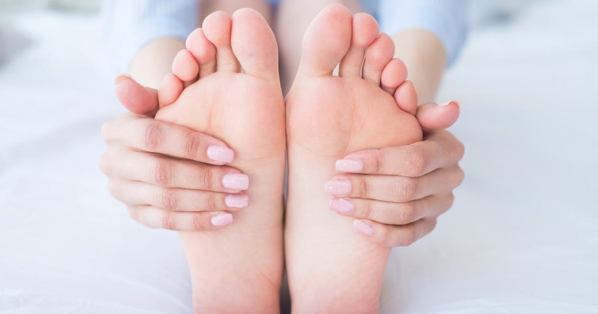 Close-up of manicured hands wrapped around the soles of bare feet